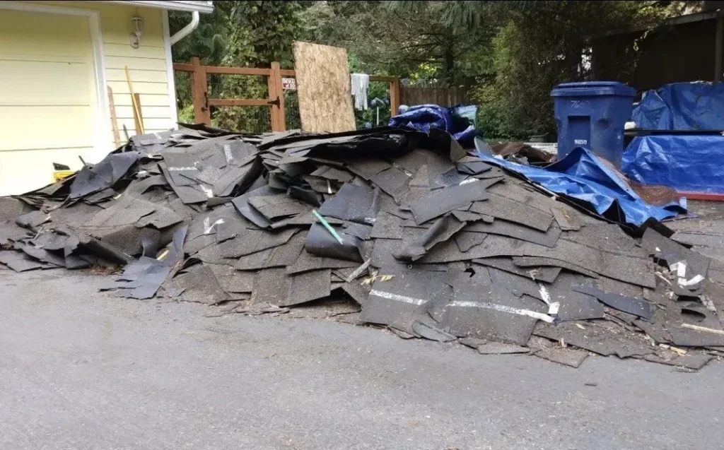 Pile of torn-off asphalt shingles and plywood beside a garage, ready for roofing debris removal in Snohomish County